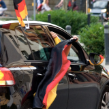 Fußballfans nehmen in einem schwarzen Auto an einer Jubelfeier teil und schwenken aus dem Fahrzeug heraus Fahnen.
